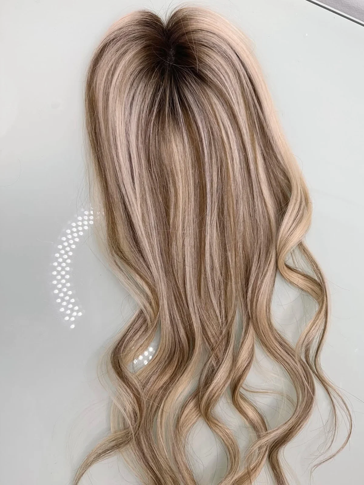 Blonde human hair topper styled in soft waves